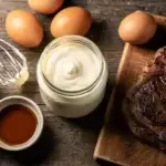 Homemade carnivore mayonnaise in a glass jar with eggs, tallow, and a steak, illustrating can you have mayo on the carnivore diet.