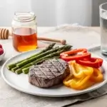 A photo illustrating what is the primal diet with a table of grass-fed steak, vegetables, nuts, and honey.